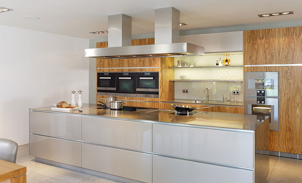 Große Beige Kücheninsel mit Herd und gegenüberliegenden Naturholz Schränken mit Küchengeräten Große Beige Kücheninsel mit Herd und gegenüberliegenden Naturholz Schränken mit Küchengeräten